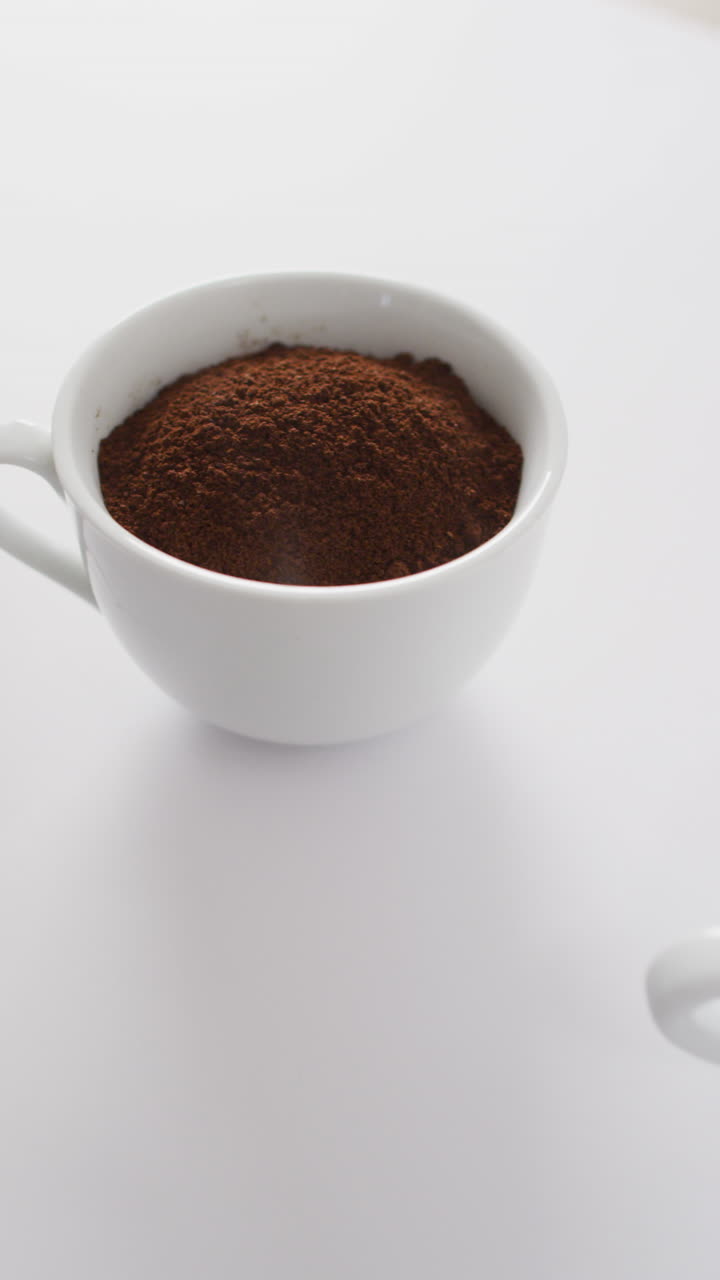 Video verticale di una tazza di chicchi di caffè, una tazza di caffè macinato e una tazza di caffè nero su un tavolo bianco