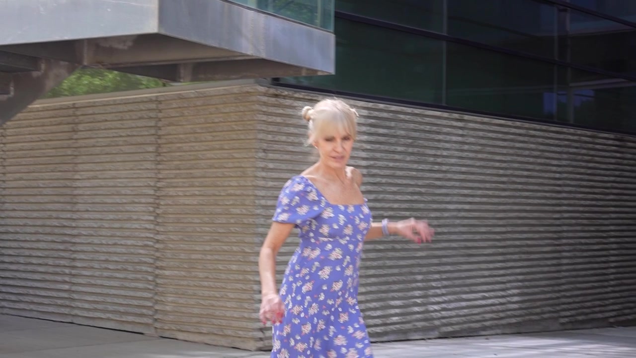 Una donna cammina con grazia con un bellissimo vestito floreale blu, circondata da architettura moderna.