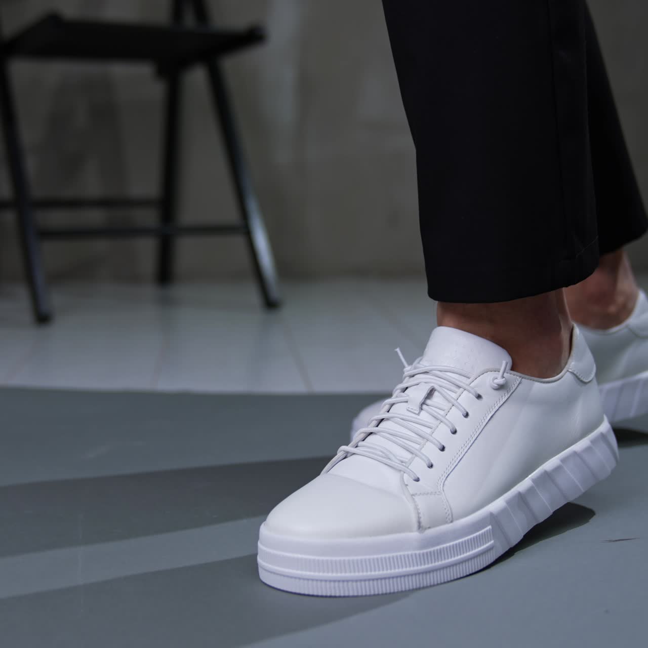 White sportive casual sneakers on male feet. Close up. Man wearing black trousers demonstrates stylish footwear