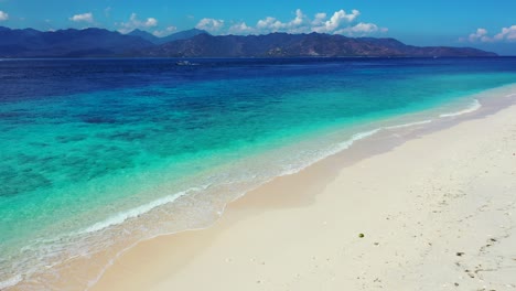 calm clear water of blue turquoise sea with white waves washing sandy beach of tropical island, bright sky over mountains in indonesia