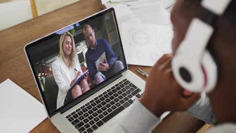 african american male college student wearing headphones having a video call on laptop at home