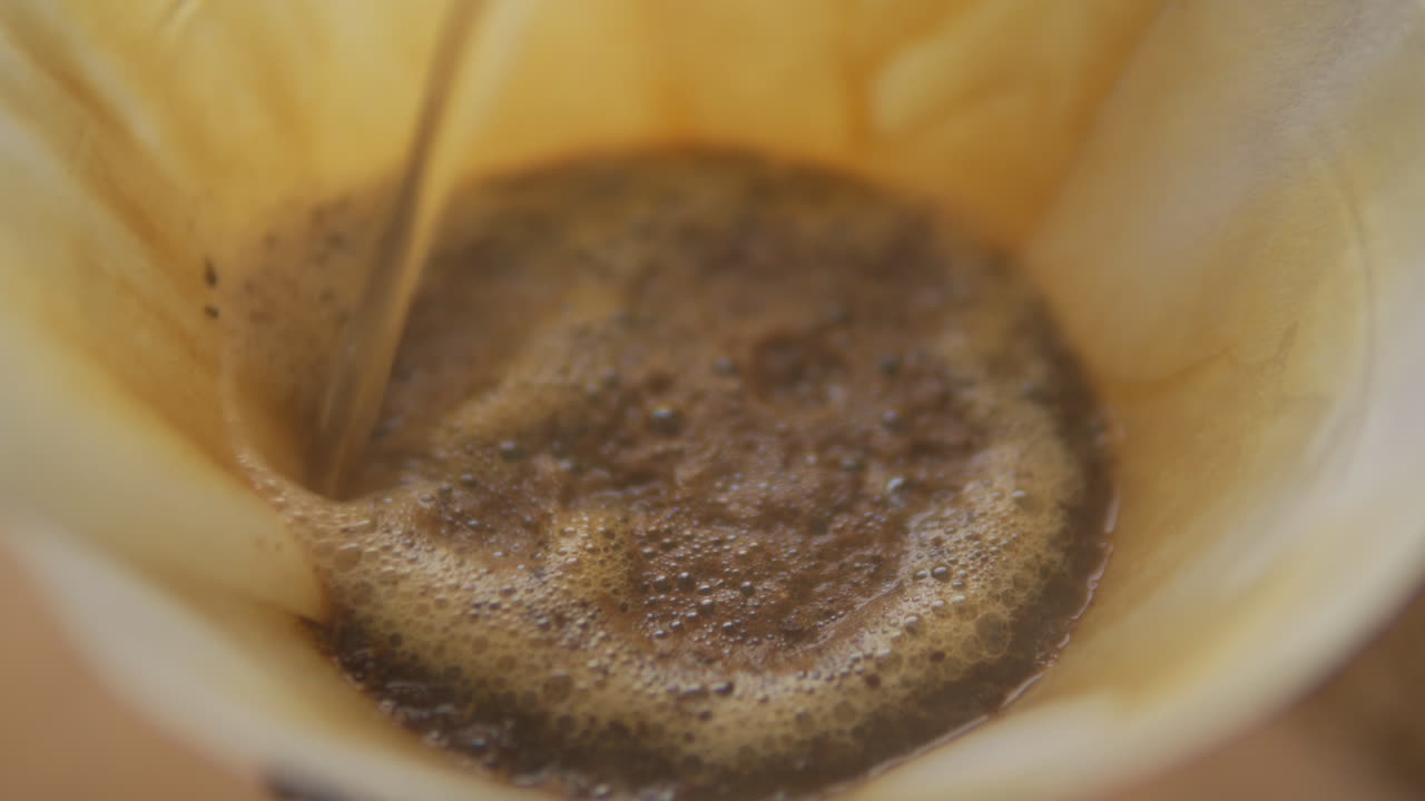 Tampilan makro jarak dekat biji kopi segar yang sudah digiling di kertas filter Chemex, disiram air panas untuk kopi yang membangkitkan energi