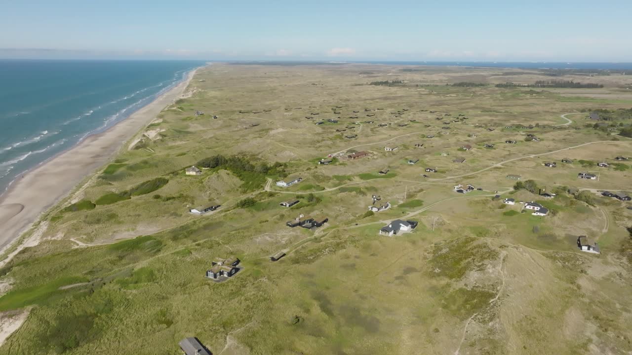 una vista aérea de casas pequeñas se alzan entre dunas de arena altas y cubiertas de hierba