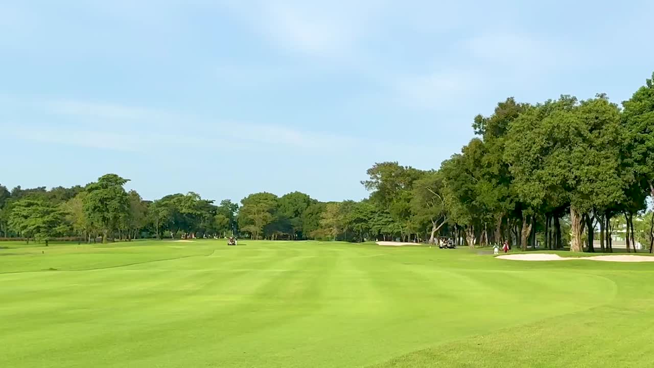 Wide view of a lush green fairway bordered by trees under a clear blue sky.