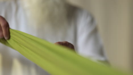 fotografía de estudio de cerca de un anciano sikh con barba plegando tela para turbante contra un fondo plano en tiempo real