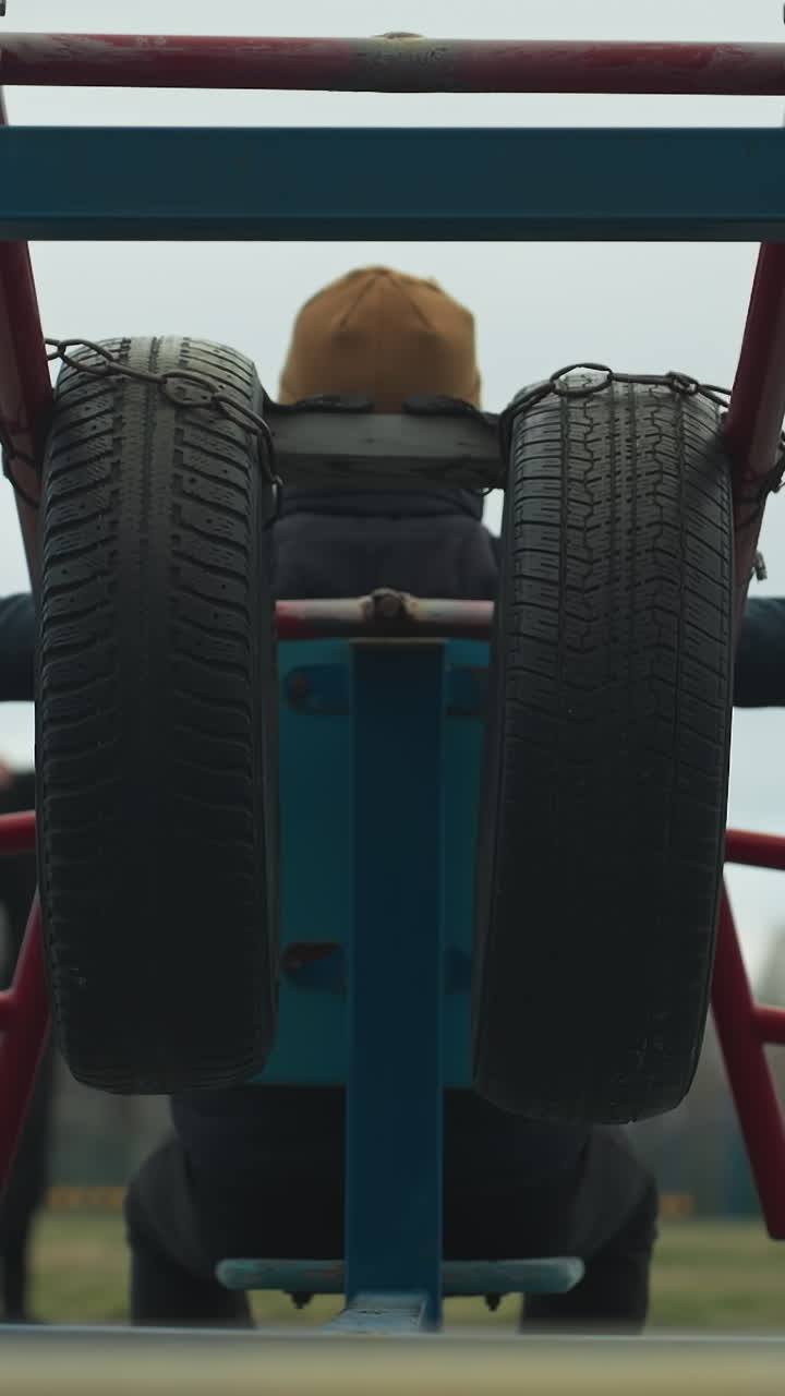 Back view of a coach stretching his hands out on workout equipment with two boys in the background, one in a gray sweater working out, with someone passing on an electric bike