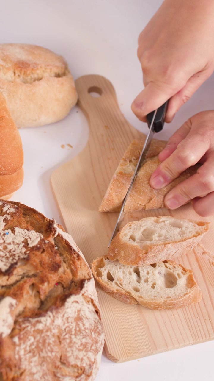 Close-up of hands using a knife to slice crusty bread on a wooden cutting board.