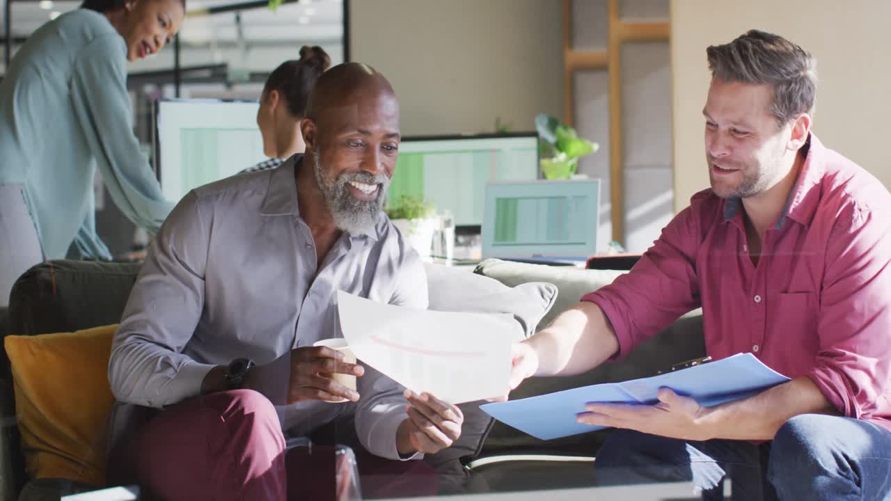 Diverse business people sitting with documents and discussing work at office