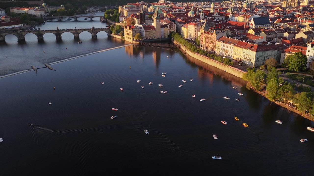 Korkealta otettu ilmakuva Vltava-joesta Kaarlensillan ja kymmenien vedessä hajallaan olevien pienten veneiden kanssa, Prahan historiallinen keskusta taustalla kultaisen tunnin aikaan, Praha