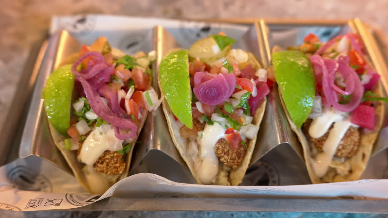 Close up of freshly prepared tacos with lime wedges, pico de gallo and pickled onions in metal taco holders