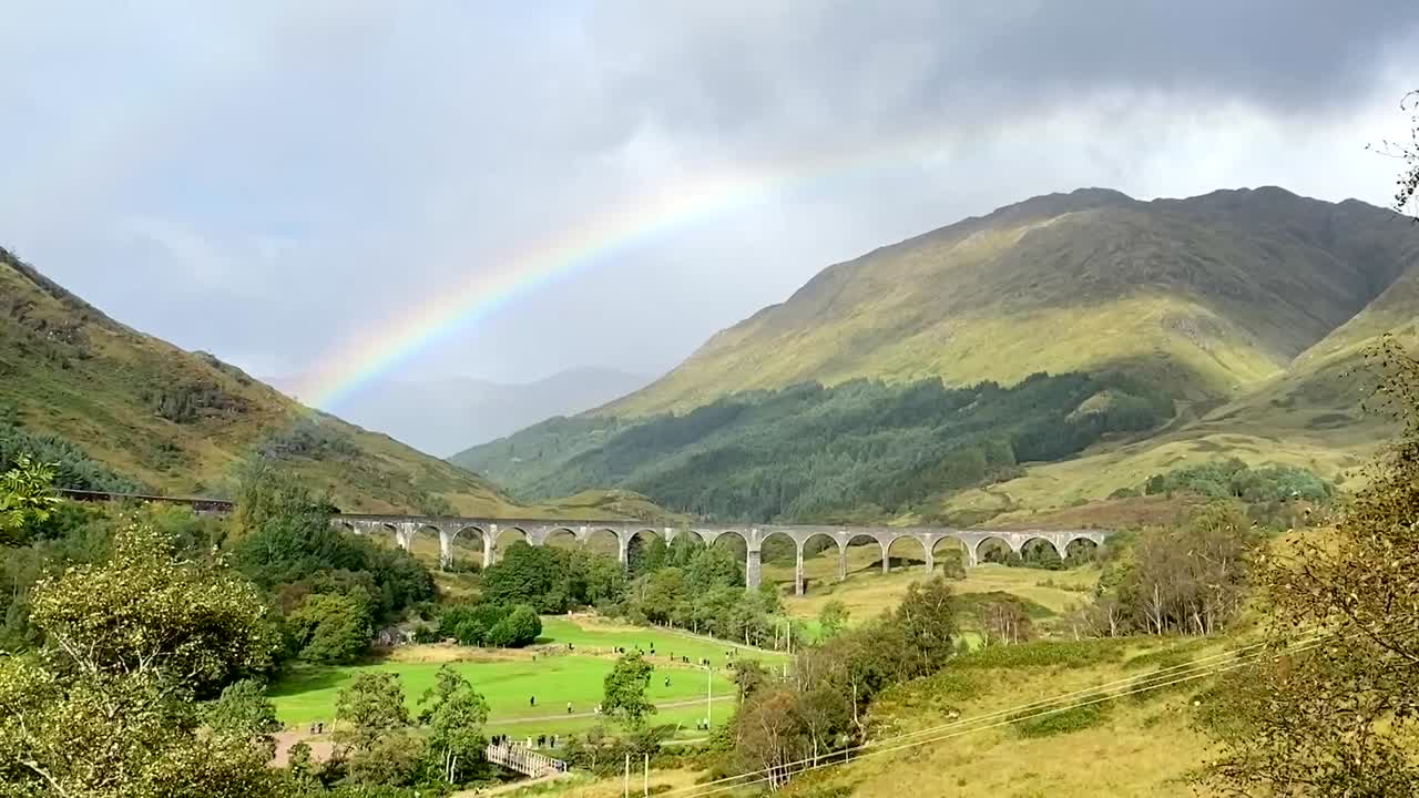 tren de vapor retro que corre en la vía del tren de arco de cemento frente a un arco iris en el valle verde