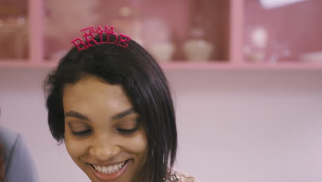 Close-Up-View-Of-Woman-With-Headdresses-And-Holding-Cardboard-Phrase-Dancing-In-A-Pink-Room-Celebrating-A-Bachelorette-Party