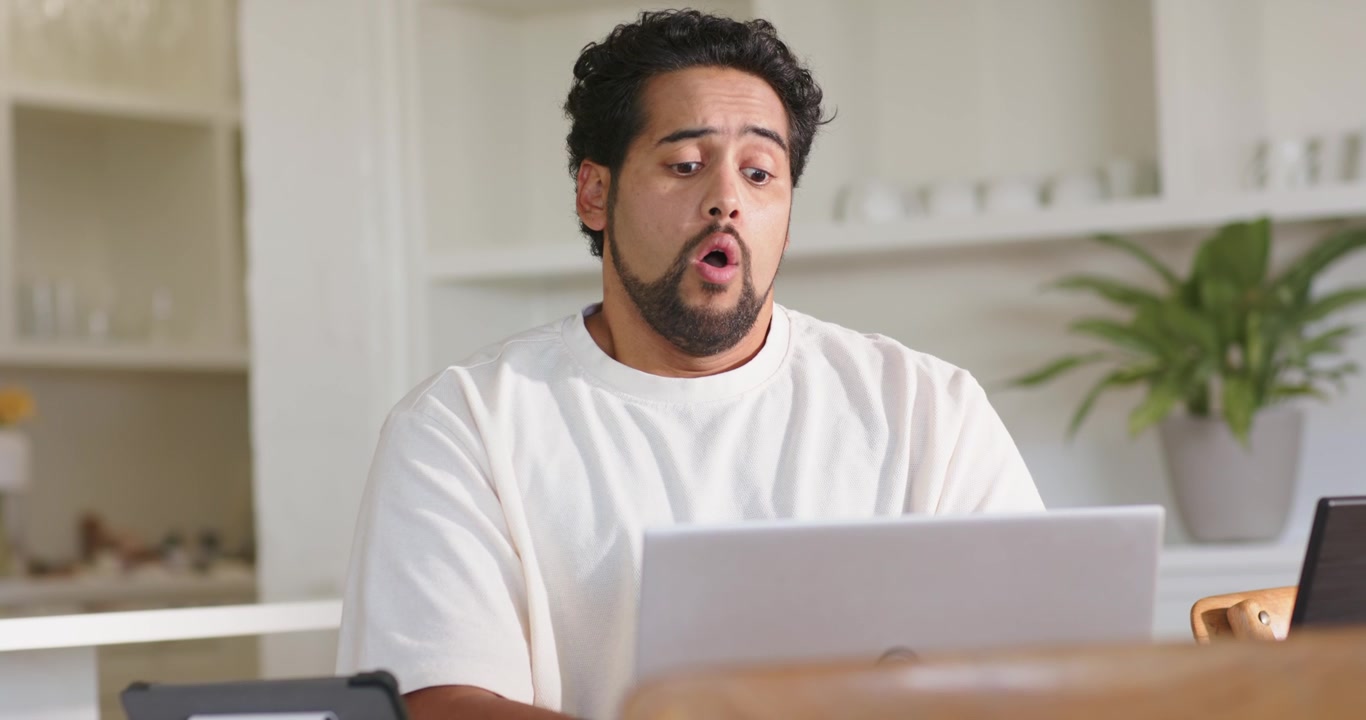 African American mid-adult male leaning, working on laptop, opening mouth, then relaxing in kitchen