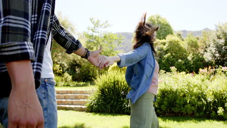 happy diverse couple holding hands and walking in sunny garden, in slow motion