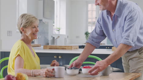 Retired-Couple-Sitting-Around-Table-At-Home-Having-Healthy-Breakfast-With-Fresh-Fruit--Together