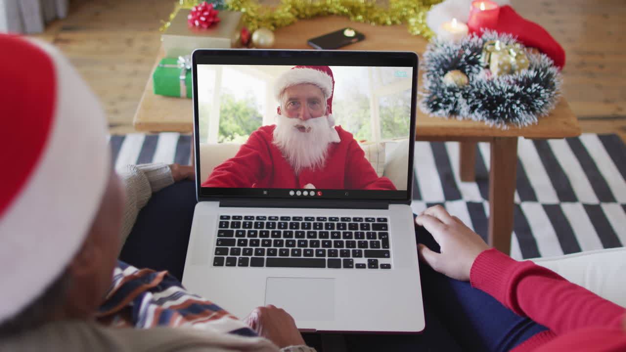 madre y hija afroamericanas usando una computadora portátil para una videollamada de navidad con santa en la pantalla