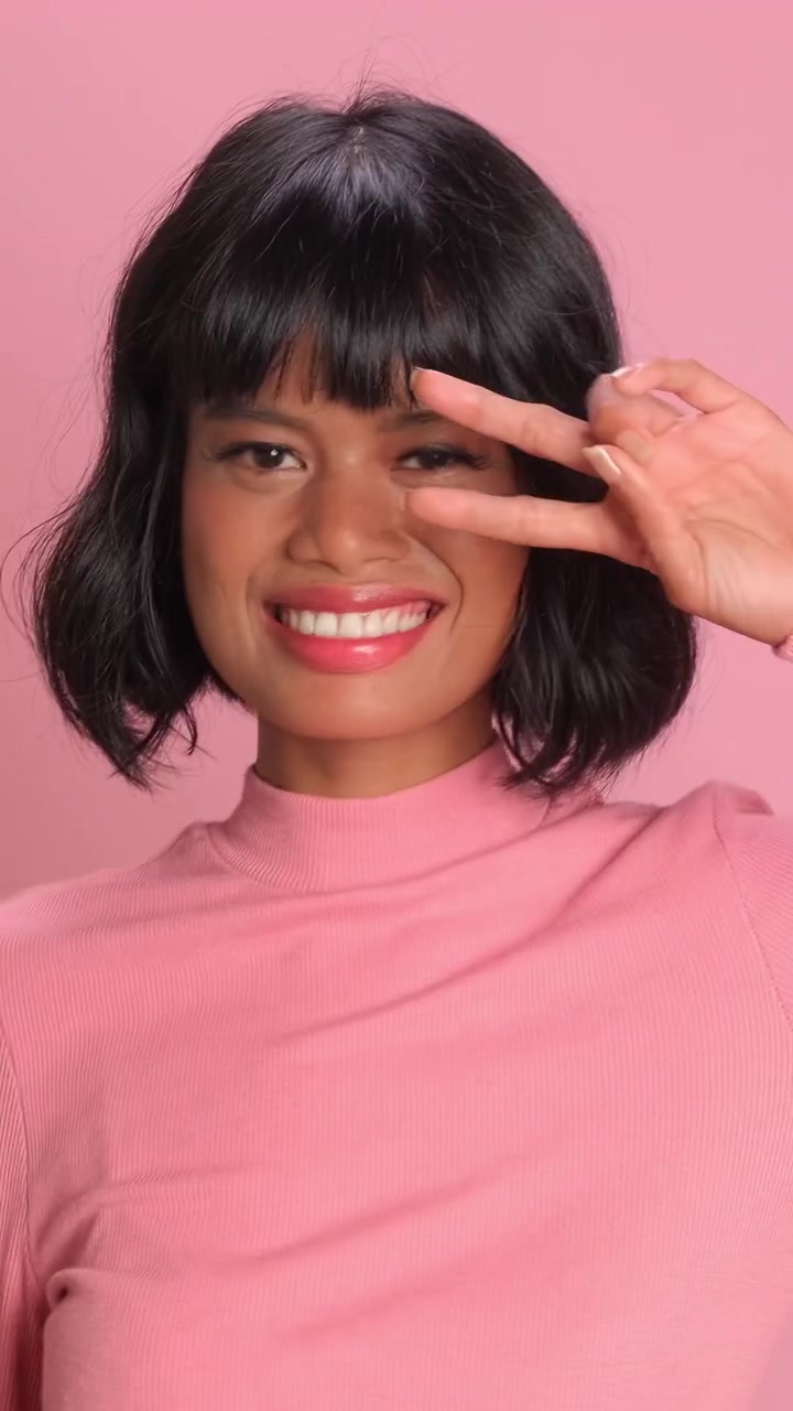 Cheerful southeast asian woman waving and smiling happily against pink studio