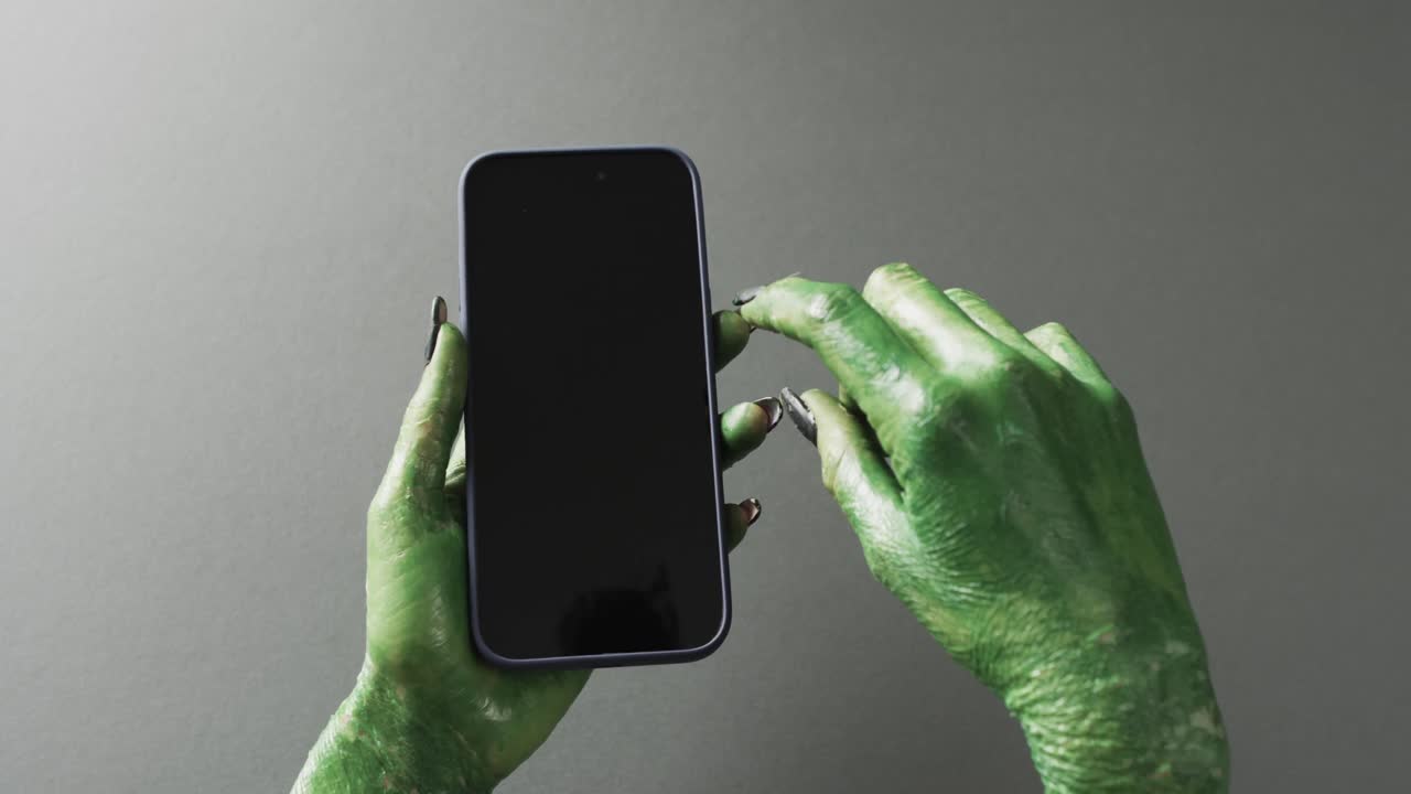 video de las manos del monstruo verde de halloween sosteniendo un teléfono inteligente con espacio de copia en un fondo gris