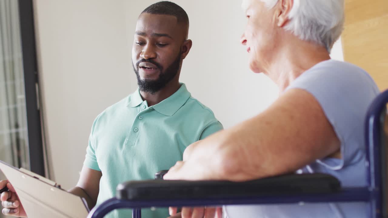 Video of african american male physiotherapist examining caucasian senior woman on wheelchair