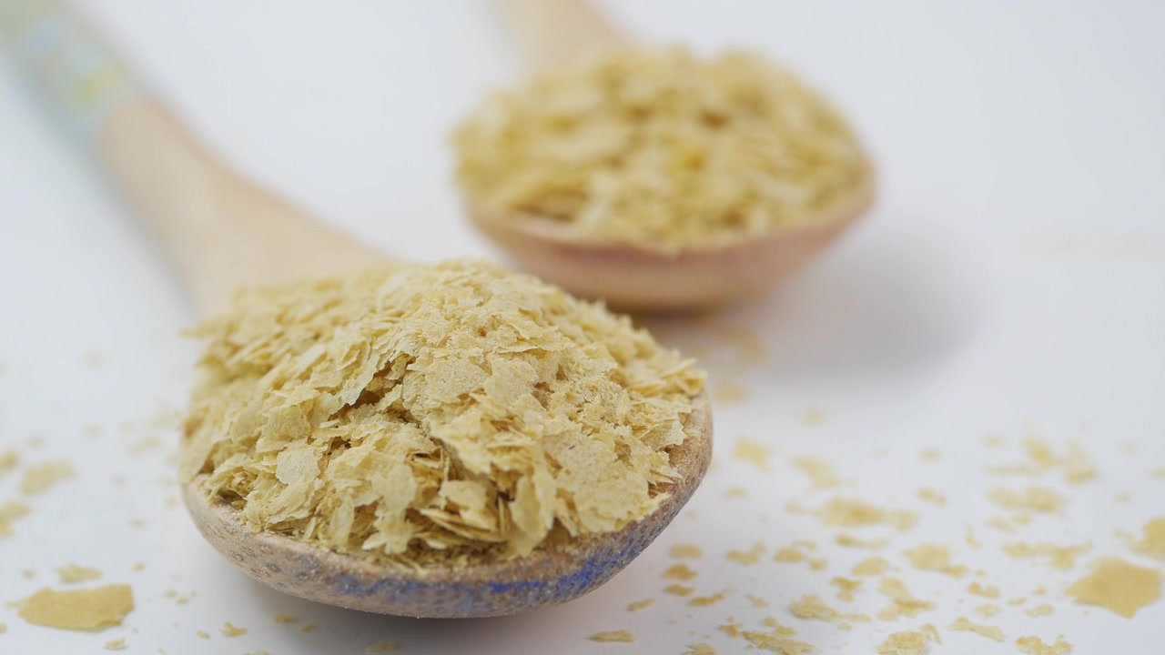 Fiocchi di lievito alimentare in cucchiai di legno su sfondo bianco