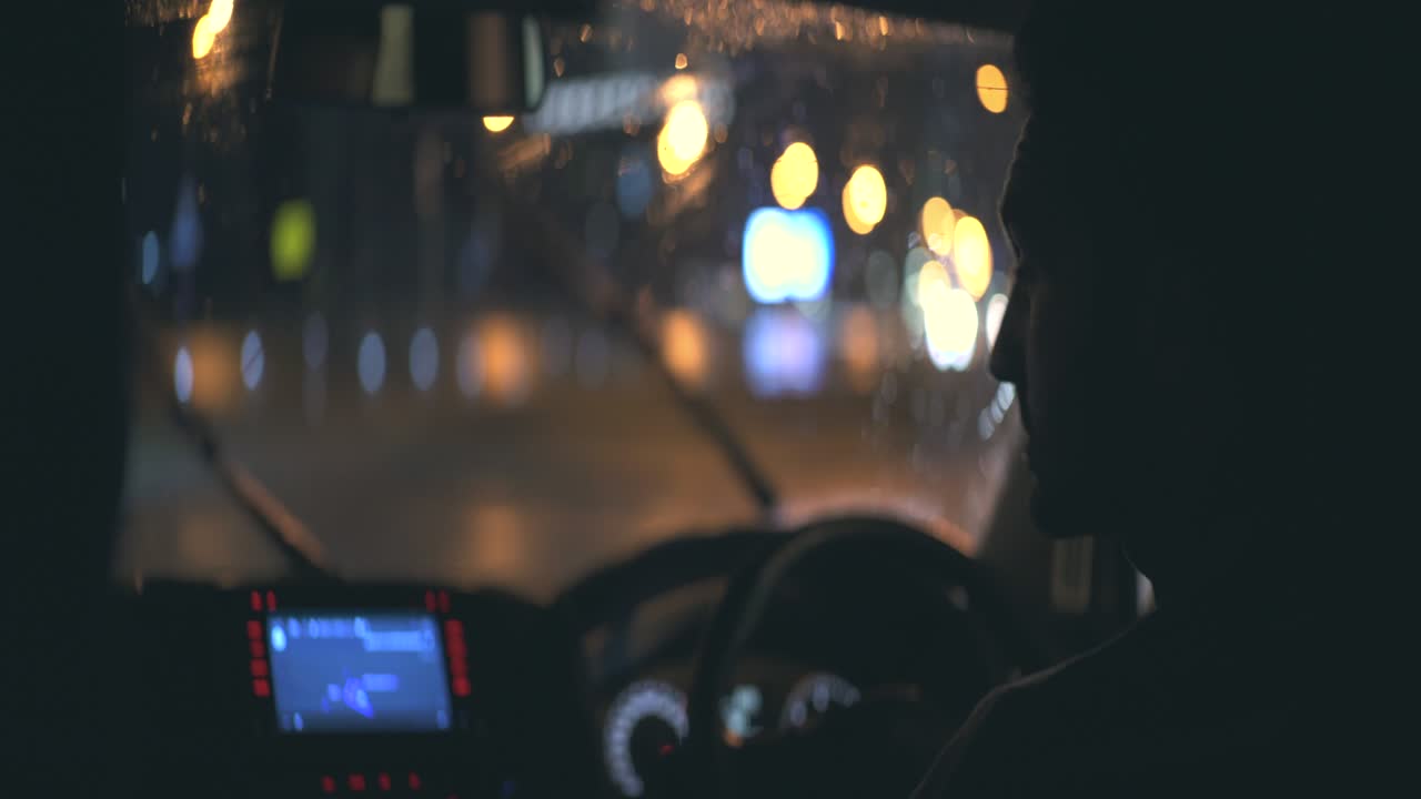 젊은이가 밤의 비가 오는 도로에서 자동차를 운전합니다.