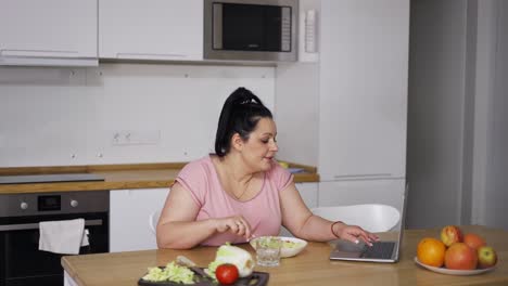 mujer con sobrepeso comiendo cereales frente a la computadora portátil