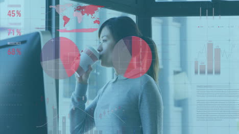 Woman drinking from paper cup in office, displaying technology charts and global data overlays