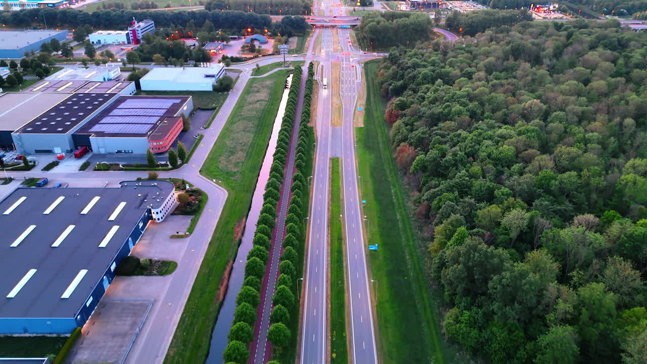 Aerial view of a highway with greenery. A wide highway runs through lush greenery, lined with trees and buildings, glowing in soft evening light