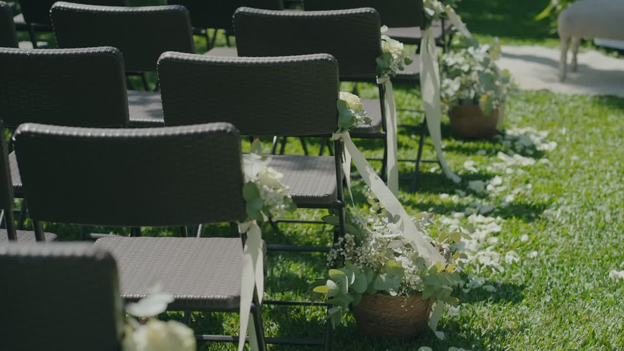 Sedie per cerimonia nuziale disposte sull'erba con decorazioni floreali lungo la navata