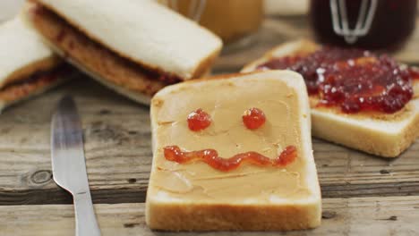 cara feliz sobre mantequilla de maní y sándwich de jalea y cuchillo de mantequilla en una bandeja de madera