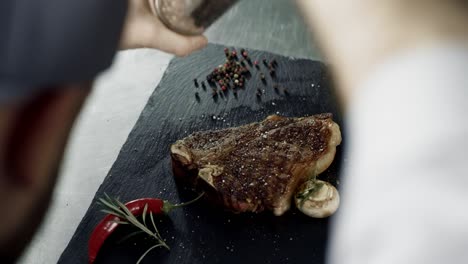 chef peppering meat at stone cutting board. man hands peppering grilled streak