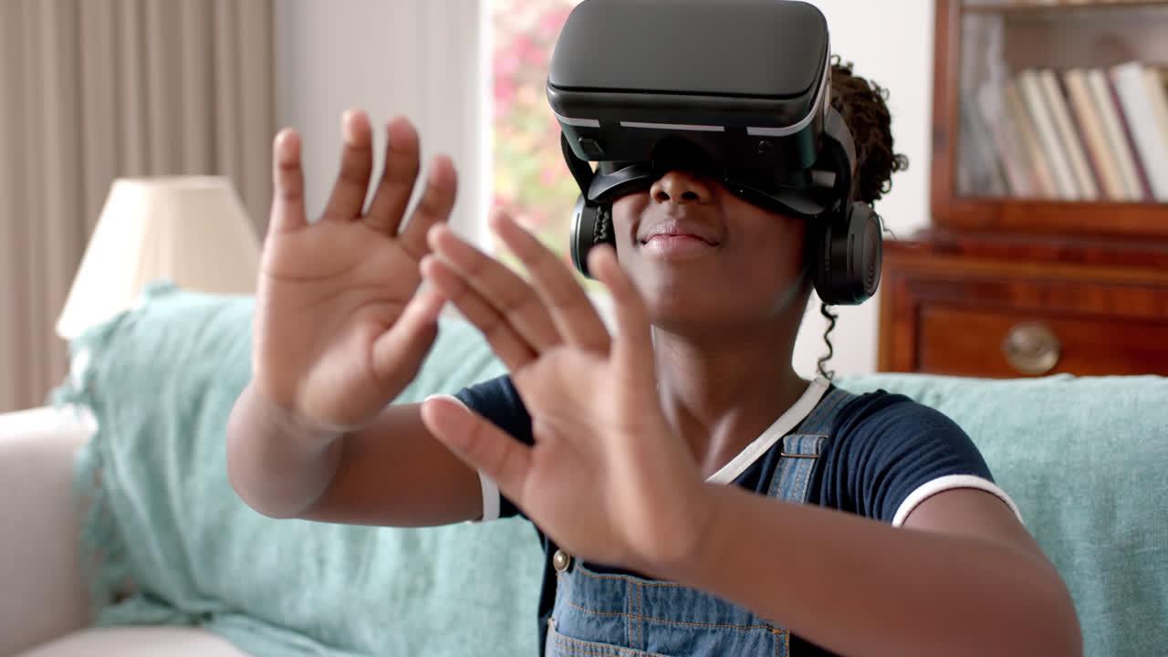 Afroamerikansk pige bruger VR-headset og rører ved virtuel skærm i stuen, slowmotion.