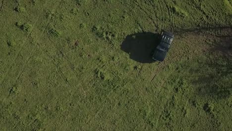 Slow-motion-top-down-aerial-drone-shot-of-classic-4wd-SUV-driving-across-green-grassy-field