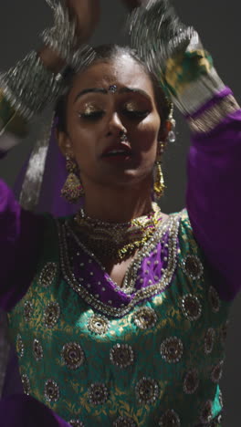 vertical video close up of female kathak dancer performing dance wearing traditional indian dress seated on floor in spotlight 1