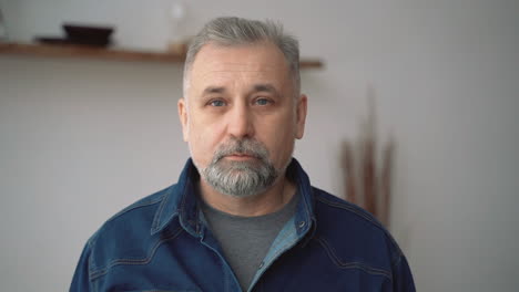 Portrait-Of-Gray-Haired-Mature-Man-With-Beard-Looking-At-Camera-Smiling-Indoors-At-Home