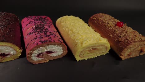 Draufsicht,-Flache-Aufnahme-Eines-Schiebereglers-Mit-Kuchenrollen,-Brazo-Gitano,-Biskuitrolle,-Dessertsammlung,-Schokolade,-Ferrero-Käse,-Butter,-Gelee,-Beeren,-Kirsche-Auf-Schwarzem-Hintergrund