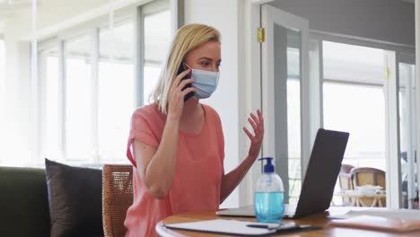 woman wearing face mask talking on smartphone at home