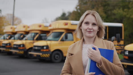 Portrait-of-a-middle-aged-teacher.-Stands-against-the-background-of-a-row-of-yellow-school-buses,-holds-a-textbook-in-his-hands