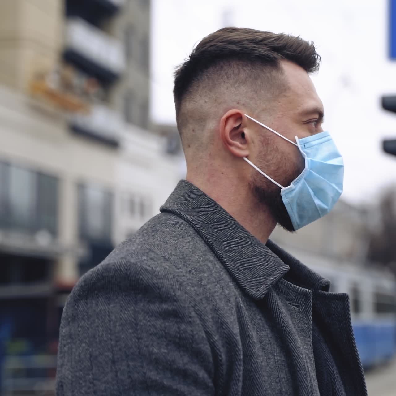 Profile view of male face in mask outdoors. Young man in protective medical mask standing near the road with city transport. Epidemic Coronavirus. Slow motion.
