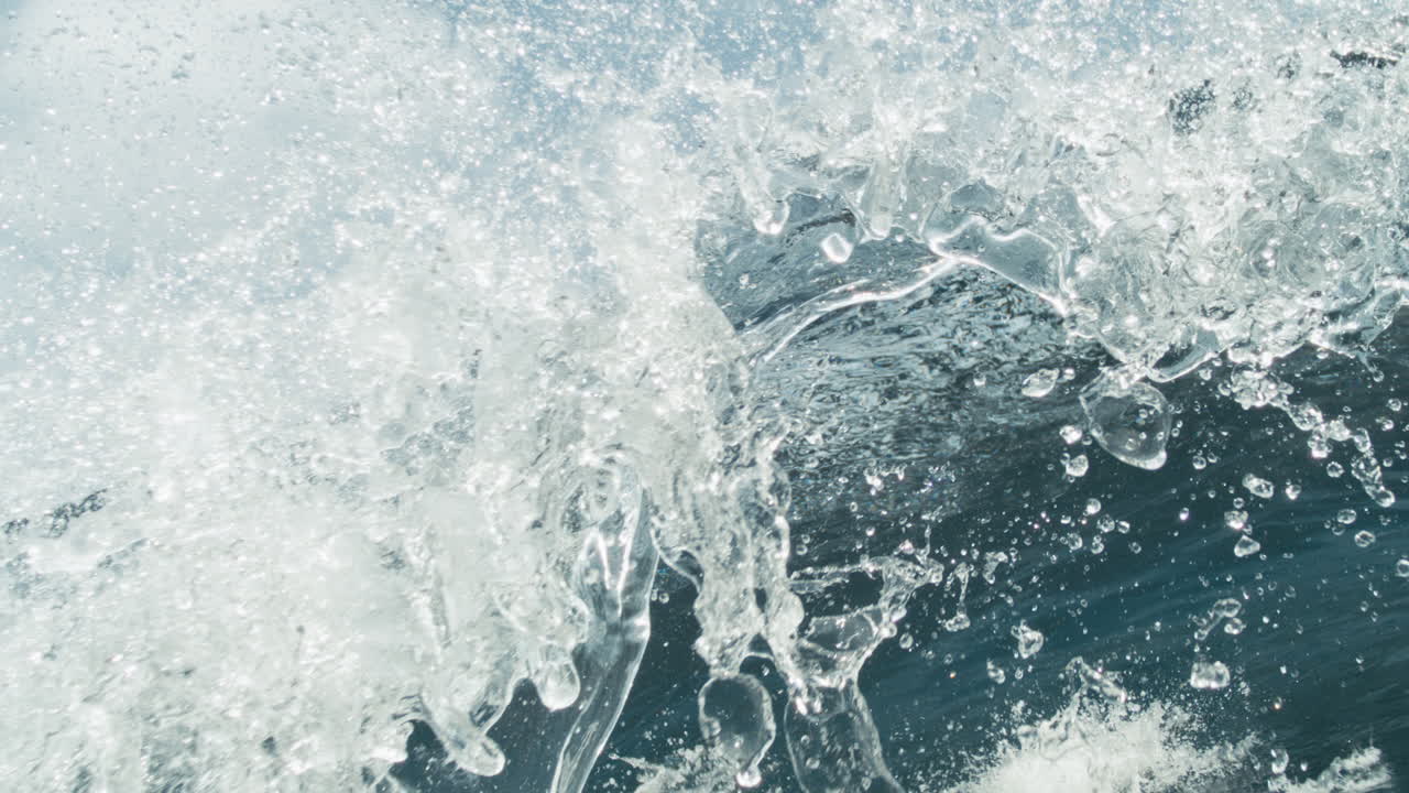Tight closeup of translucent wave cresting and splashing in sunlight