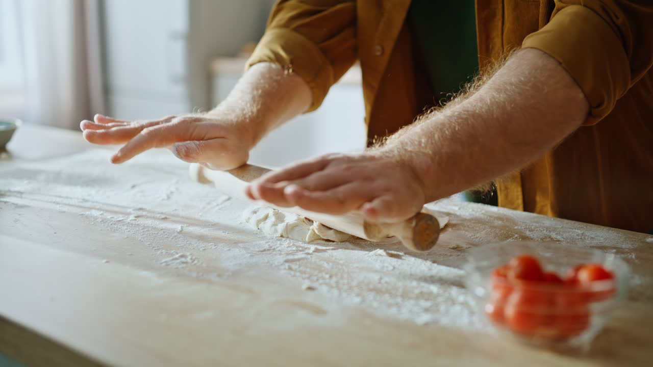 Primo piano di un uomo che aggiunge farina di grano all'impasto del pane fatto in casa su un piano di lavoro in legno
