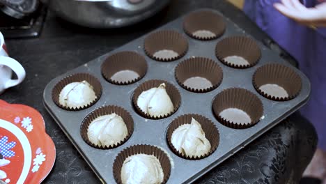 close up of a pastry chef using an ice cream scoop to meticulously fill a cupcake tray with batter, preparing for baking