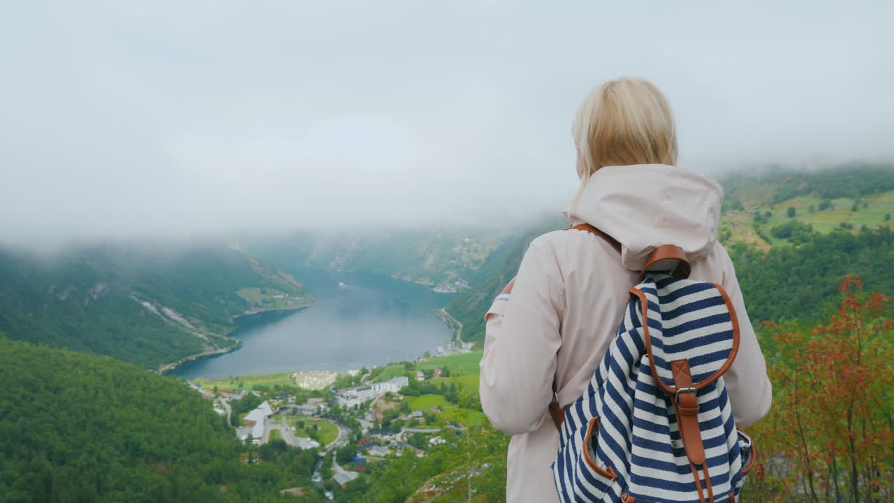 женщина с рюкзаком любуется прекрасным видом на фьорд, открывающимся со знаменитой летающей скалы в ноу