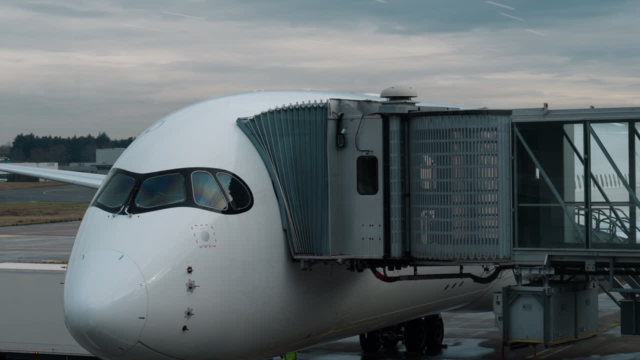 Primo piano di un moderno aereo commerciale parcheggiato al gate di un aeroporto e collegato a un finger, che mostra l'infrastruttura aeronautica, il trasporto aereo e le operazioni aeroportuali
