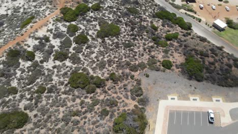 Drone-Aéreo-Girando-Y-Elevándose-Desde-Una-Autocaravana-Y-Un-Estacionamiento-Hasta-Una-Hermosa-Playa