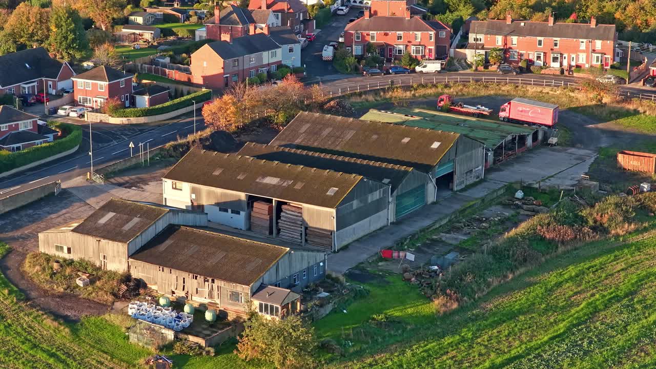 Cluster of farm sheds and storage buildings in Hemingfield, South Yorkshire, with open yard, agricultural equipment, and green fields under morning light seen from above