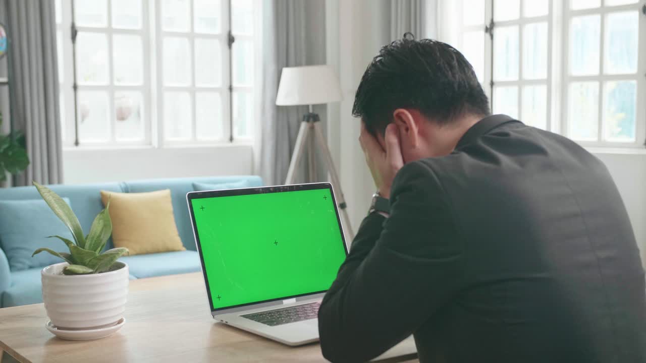 un hombre de negocios asiático con traje de negocios está cansado después de escribir en la computadora de pantalla verde mientras trabaja en casa.