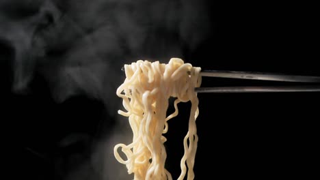 chopsticks lifting up the instant noodle with steam and smoke on black background