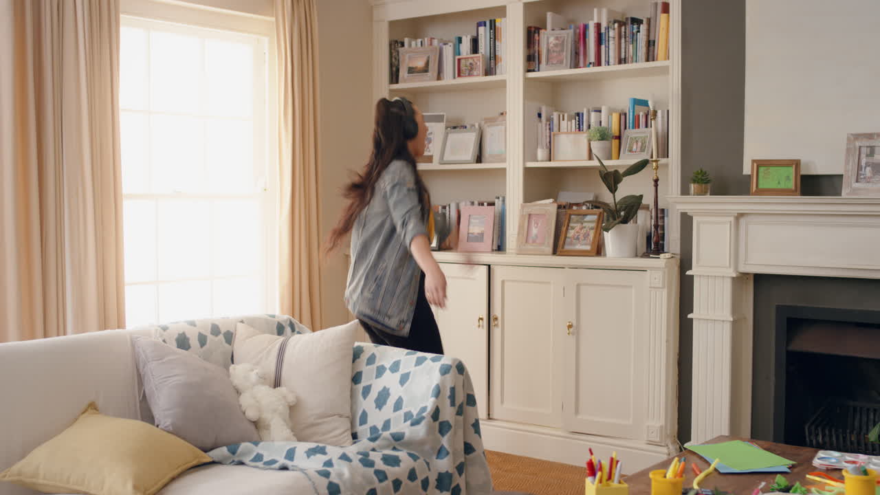 재미있는 젊은 여성이 헤드폰을 착용하여 춤을 추고 음악을 듣고 재미있는 십대 소녀가 집에서 멋진 춤 움직임으로 축하하고 주말 4k에서 자유를 즐기고 있습니다.