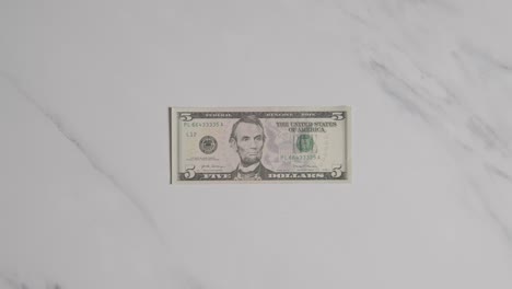 Overhead-Currency-Shot-Of-Hand-Grabbing-US-5-Dollar-Bill-On-Marble-Surface-1